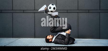 Bild eines Geschäftsmanns und Freispielers, der mit dem Ball auf der Straße Tricks macht. Konzept über Sport- und Geschäftsleute Stockfoto