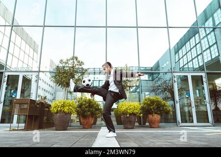 Bild eines Geschäftsmanns und Freispielers, der mit dem Ball auf der Straße Tricks macht. Konzept über Sport- und Geschäftsleute Stockfoto
