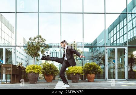 Bild eines Geschäftsmanns und Freispielers, der mit dem Ball auf der Straße Tricks macht. Konzept über Sport- und Geschäftsleute Stockfoto