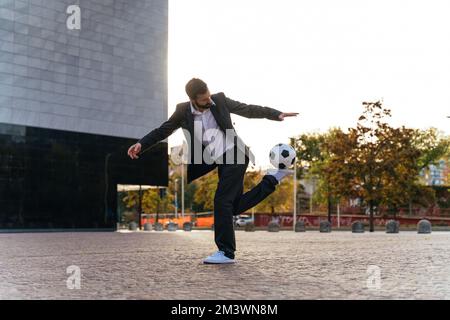 Bild eines Geschäftsmanns und Freispielers, der mit dem Ball auf der Straße Tricks macht. Konzept über Sport- und Geschäftsleute Stockfoto