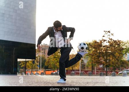Bild eines Geschäftsmanns und Freispielers, der mit dem Ball auf der Straße Tricks macht. Konzept über Sport- und Geschäftsleute Stockfoto