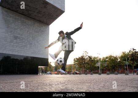 Bild eines Geschäftsmanns und Freispielers, der mit dem Ball auf der Straße Tricks macht. Konzept über Sport- und Geschäftsleute Stockfoto