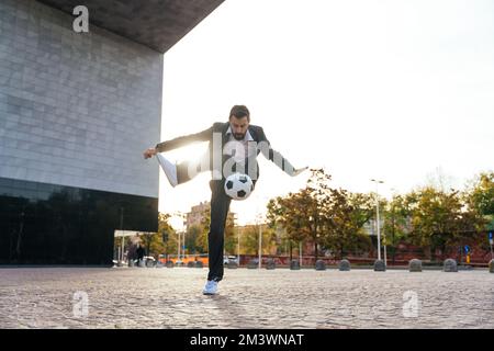 Bild eines Geschäftsmanns und Freispielers, der mit dem Ball auf der Straße Tricks macht. Konzept über Sport- und Geschäftsleute Stockfoto