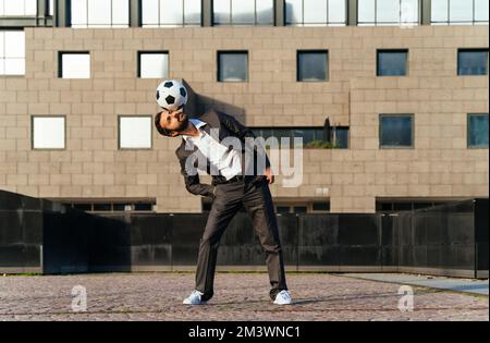 Bild eines Geschäftsmanns und Freispielers, der mit dem Ball auf der Straße Tricks macht. Konzept über Sport- und Geschäftsleute Stockfoto
