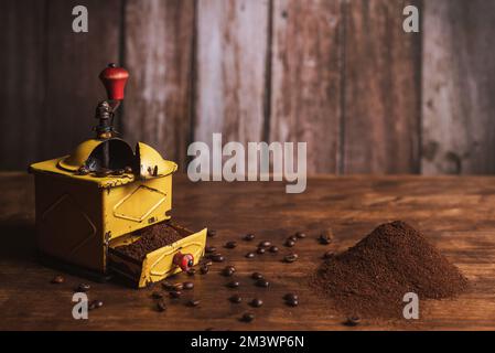 Kaffeemühle neben einem kleinen Berg gemahlenen Kaffees und verstreuten Kaffeebohnen auf dem Holztisch Stockfoto