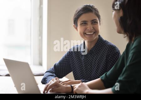 Glückliche junge indische Mitarbeiterin, die mit einem Kollegen spricht Stockfoto