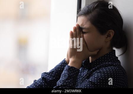 Frustrierte, unglückliche, junge Indianerin, die am Fenster weint Stockfoto
