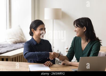 Fröhliche, multiethnische Kollegen, die sich an einem gemeinsamen Arbeitsplatz die Hände schütteln Stockfoto
