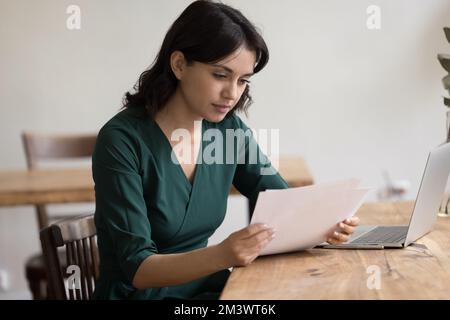 Fokussierte, ziemlich freiberufliche Mitarbeiterin, die am Tisch des Heimbüros sitzt Stockfoto