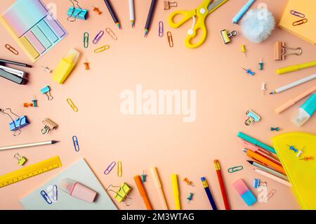 Kreativer Schülerschreibtisch mit Schulbedarf und Kopierbereich in der Mitte. Draufsicht oder flach liegend. Trendige Wohnung für den Schulanfang lag auf pfirsichrosa Hintergrund Stockfoto