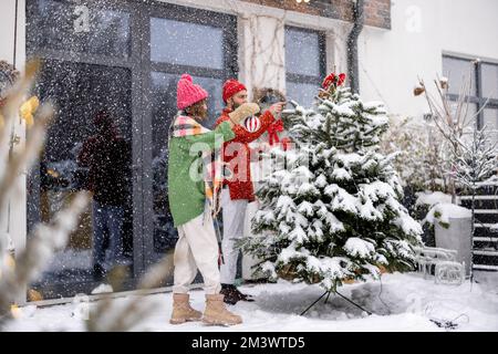 Ein junges Paar schmückt den Weihnachtsbaum im Garten Stockfoto