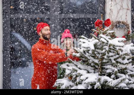 Ein junges Paar schmückt den Weihnachtsbaum im Garten Stockfoto