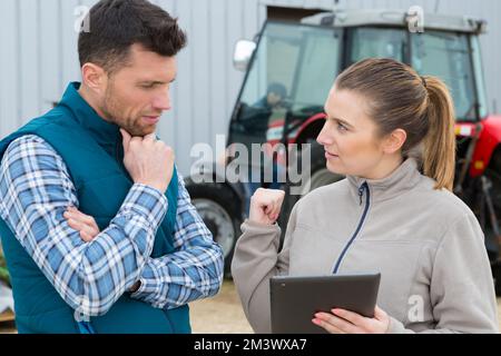 Männliche und weibliche Bauern, die sich neben einem Traktor unterhalten Stockfoto
