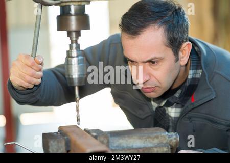 Mann, der den Bohrer auf Metall absenkt Stockfoto