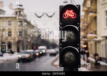 Ampel für Fahrräder mit Fahrradsymbol und aktivem rotem Licht, das am Wintertag den Hintergrund der Stadt beleuchtet Stockfoto