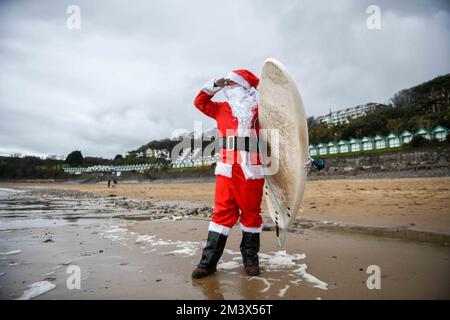 Der Surfer Andy Parkinson stellte sich vor, wie er während des alljährlichen Santa Surf Events am Gower Beach in Langland Bay, Swansea, in das eisige kalte Wasser fuhr, um Geld für Surfer gegen die Kanalisation zu sammeln und den Surfern dabei zu helfen, in Weihnachtsstimmung zu kommen. Stockfoto