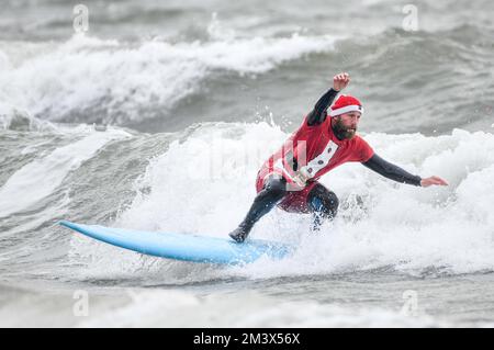 Spendensammler trotzen dem eisigen Wasser in Langland Bay, Swansea, während der alljährlichen Santa Surf Veranstaltung, die jedes Jahr am Gower Beach stattfindet, um Geld für Surfer gegen die Kanalisation zu sammeln und den lokalen Surfern dabei zu helfen, in Weihnachtsstimmung zu kommen. Stockfoto