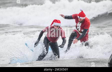 Spendensammler trotzen dem eisigen Wasser in Langland Bay, Swansea, während der alljährlichen Santa Surf Veranstaltung, die jedes Jahr am Gower Beach stattfindet, um Geld für Surfer gegen die Kanalisation zu sammeln und den lokalen Surfern dabei zu helfen, in Weihnachtsstimmung zu kommen. Stockfoto