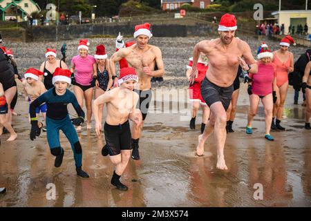 Vor dem alljährlichen Santa Surf Event, das jedes Jahr am Gower Beach stattfindet, um Geld für wohltätige Zwecke zu sammeln und den Surfern vor Ort in Weihnachtsstimmung zu verhelfen, drängen sich die Menschen in die eisige Kälte der Langland Bay, Swansea. Stockfoto