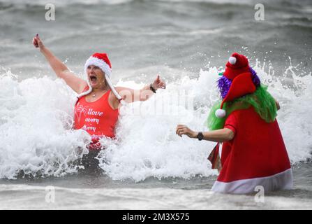 Spendensammler trotzen dem eisigen Wasser in Langland Bay, Swansea, während der alljährlichen Santa Surf Veranstaltung, die jedes Jahr am Gower Beach stattfindet, um Geld für Surfer gegen die Kanalisation zu sammeln und den lokalen Surfern dabei zu helfen, in Weihnachtsstimmung zu kommen. Stockfoto