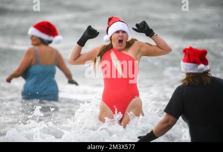 Spendensammler trotzen dem eisigen Wasser in Langland Bay, Swansea, während der alljährlichen Santa Surf Veranstaltung, die jedes Jahr am Gower Beach stattfindet, um Geld für Surfer gegen die Kanalisation zu sammeln und den lokalen Surfern dabei zu helfen, in Weihnachtsstimmung zu kommen. Stockfoto