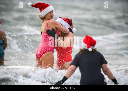 Spendensammler trotzen dem eisigen Wasser in Langland Bay, Swansea, während der alljährlichen Santa Surf Veranstaltung, die jedes Jahr am Gower Beach stattfindet, um Geld für Surfer gegen die Kanalisation zu sammeln und den lokalen Surfern dabei zu helfen, in Weihnachtsstimmung zu kommen. Stockfoto