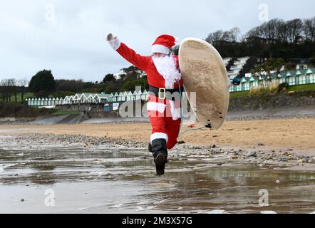 Der Surfer Andy Parkinson stellte sich vor, wie er während des alljährlichen Santa Surf Events am Gower Beach in Langland Bay, Swansea, in das eisige kalte Wasser fuhr, um Geld für Surfer gegen die Kanalisation zu sammeln und den Surfern dabei zu helfen, in Weihnachtsstimmung zu kommen. Stockfoto