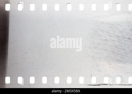 Staubige und schmutzige 35-mm-Filmtextur oder -Oberfläche. Perforierter, zerkratzter Kamerafilm isoliert auf weißem Hintergrund. Stockfoto