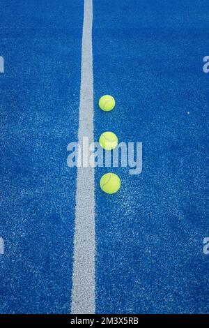 Ein vertikaler Schuss von drei Paddle-Tennisbällen auf einem blauen Kunstrasenplatz Stockfoto