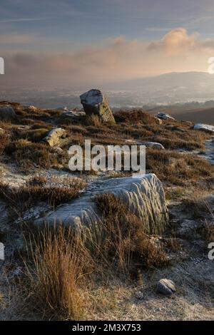 Frostbedeckte Felsen im Moor mit Blick auf Burley-in-Wharfedale in West Yorkshire, Großbritannien Stockfoto