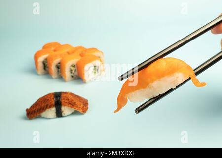 Sushi-Set und schwarze Essstäbchen auf blauem Hintergrund. Traditionelle japanische Küche. Asiatisches Essen Stockfoto