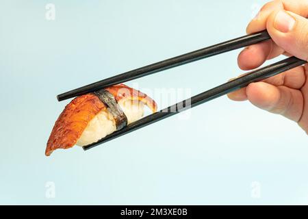 Sushi Nigiri mit Aal Unagi auf blauem Hintergrund. Traditionelle japanische Küche. Sushi-Nahaufnahme. Sushi auf Stäbchen in der Hand Nahaufnahme. Stockfoto