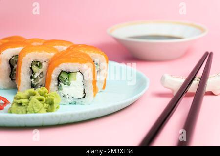 Sushi rollt philadelphia auf einem blauen Teller mit pinkfarbenem Hintergrund. wasabi Ingwer und Sauce Stäbchen. Brötchen mit Lachs, Frischkäse, Avocado. Stockfoto