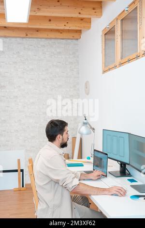 Vertikale Aufnahme eines jungen Unternehmers, der in einem modernen Büro zu Hause mit seinem Computer arbeitet. Stockfoto