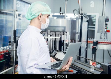 Mitarbeiter der Lebensmittel- und Getränkeindustrie, die an der Produktionslinie für Förderbänder in der Getränkeherstellung mit einem sauberen und hygienischen Bereich arbeiten. Stockfoto