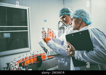 Mitarbeiter der Lebensmittel- und Getränkeindustrie, die an der Produktionslinie für Förderbänder in der Getränkeherstellung mit einem sauberen und hygienischen Bereich arbeiten. Stockfoto