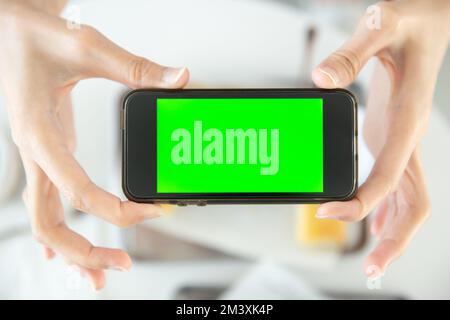 Nahaufnahme Hand halten Smartphone Draufsicht im Restaurant mit leerem Bereich grüner Bildschirm Stockfoto