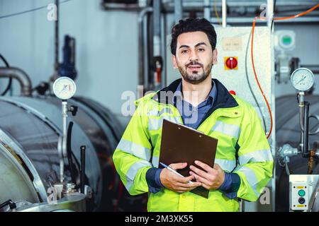 Hispanischer, intelligenter, selbstbewusster Ingenieur, männlicher Servicemitarbeiter im Fabrikporträt im Kesselwasserrohrraum. Stockfoto