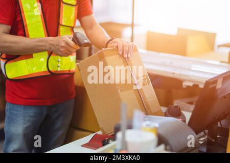 Der Mitarbeiter prüft das Postetikett mit dem Laser-Barcode-Scanner auf dem Produktkarton, um die Lieferung an den Online-Bestellkunden zu erhalten. Stockfoto