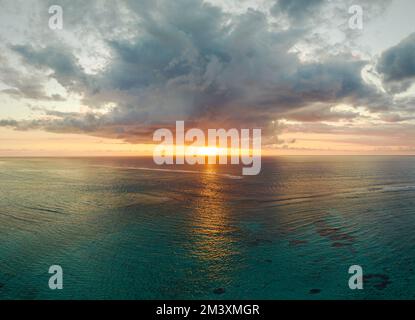 Die Sonne scheint zwischen den Wolken und dem Ozean bei Sonnenuntergang. Der Sonnenschein reflektiert sich im Wasser. das meer hat eine wunderschöne, saubere blaue Farbe. Stockfoto