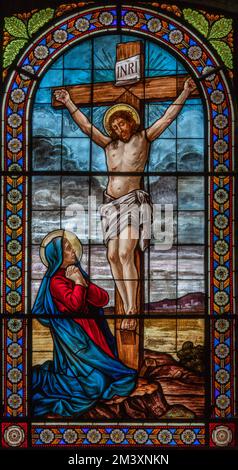 DOMODOSSOLA, ITALIEN - 19. JULI 2022: Kreuzigung und Mutter Maria auf dem Buntglas in der Kirche Chiesa dei Santi Gervasio e Protasio Stockfoto