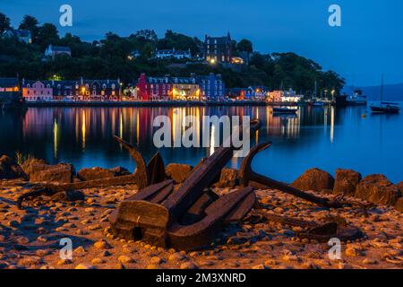 Anker am Kai mit den farbenfrohen Lichtern der Uferpromenade, die sich im stillen Wasser des Tobermory Harbour, Isle of Mull, Schottland, Großbritannien, spiegeln Stockfoto