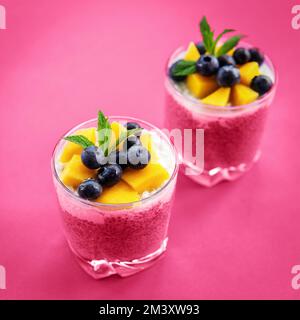 Zwei Gläser Chia-Pudding mit Kokosnusscreme, Mango und Blaubeere auf violettem Hintergrund, Draufsicht. Gesundes Essen, roh, vegan. Bild mit Tonwertkorrektur. Stockfoto