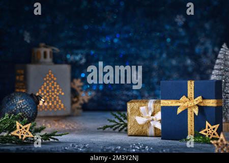 Weihnachtshintergrund in Blau und Gold. Luxuriöse Geschenke in Schachteln mit Bändern auf einem Tisch mit Laterne. Stockfoto