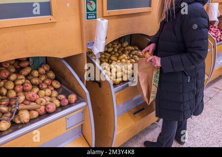 Nahaufnahme einer Frau, die Kartoffeln in eine Papiertüte pflückt, im Gemüsebereich des Supermarkts. Schweden. Uppsala. Stockfoto