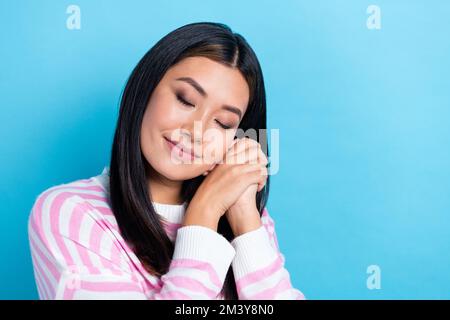 Nahaufnahme Foto eines jungen süßen, hübschen, entspannten koreanischen Lady Schwarzes Haar tragen gestreiftes Hemd Hände zusammen schlafen nach der Arbeit isoliert auf blauem Hintergrund Stockfoto