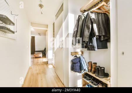 Ein begehbarer Kleiderschrank mit Kleidungsstücken an der Wand und Kleiderständer mit Mänteln, Schuhen und anderen Gegenständen Stockfoto