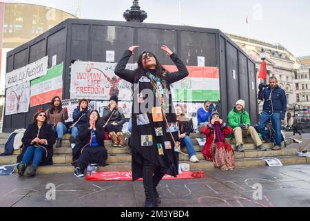 London, Großbritannien. 17.. Dezember 2022 Eine Demonstrantin tanzt mit einer Schlinge um ihren Hals und Fotos von im Iran inhaftierten Demonstranten auf ihrem Mantel. Eine Gruppe von Frauen inszenierte eine Demonstration und Aufführung im Piccadilly Circus, um gegen die berichteten Hinrichtungen regierungsfeindlicher Demonstranten im Iran zu protestieren. Die Aktivisten haben sich Seile um den Hals gebunden und ihre Hände mit falschem Blut bedeckt. Kredit: Vuk Valcic/Alamy Live News Stockfoto