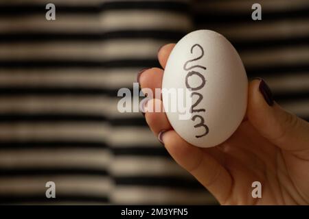 Die Hand einer Frau hält ein Ei mit der Inschrift 2023 auf einem gestreiften Hintergrund, frohes neues Jahr 2023, Essen Stockfoto