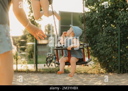 Ein kleines Mädchen in einem Kleid saugt am warmen Sommerabend ihren Daumen an einer Schaukel Stockfoto